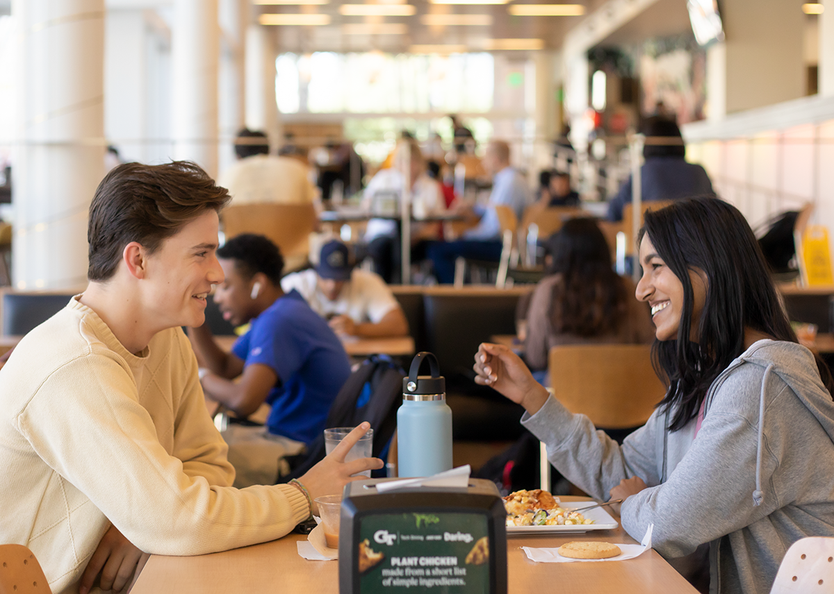 A guy and a gal smiling while eating at the North Ave Dining Hall.
